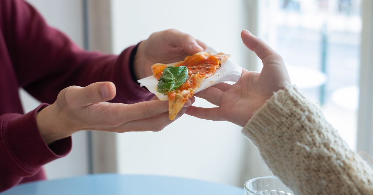 Two people enjoying and sharing a slice of delicious pizza in a cozy indoor setting.